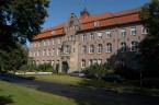 großes altes Gebäude mit rotem Dach und Bäumen im Vordergrund